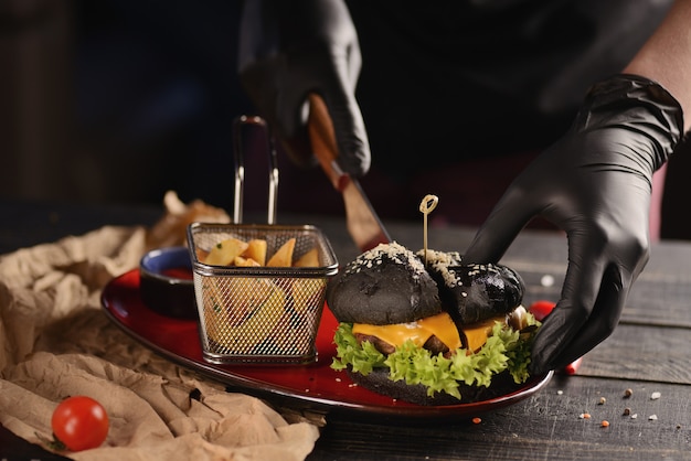 Black burger with fries and sauce. In a red plate on a wooden table