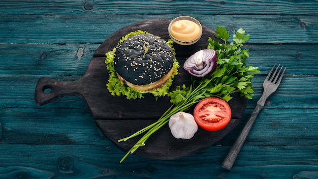 Фото Черный бургер с мясным луком и салатом на деревянном фоне вид сверху копией пространства
