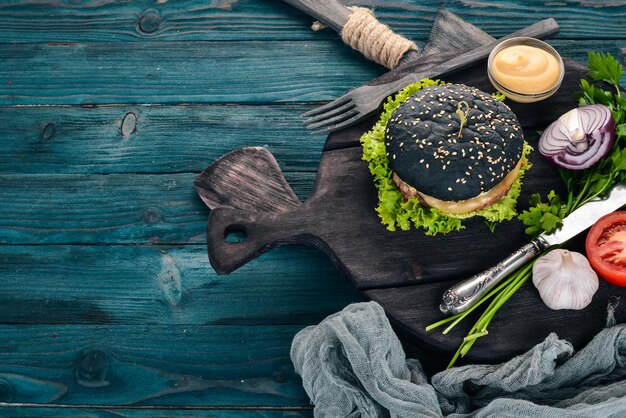 Black burger with meat, onion and lettuce. On a wooden background. Top view. Copy space.