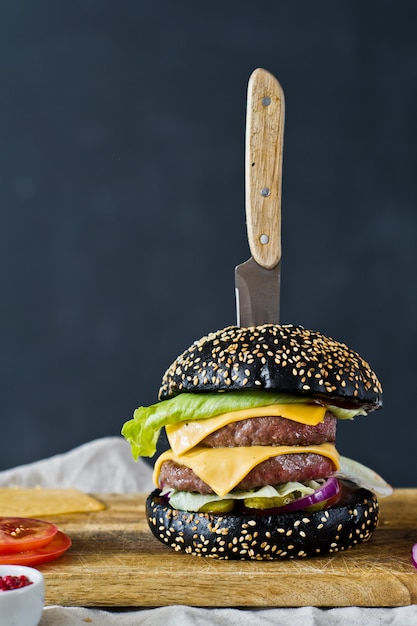 Black Burger on a wooden chopping Board.