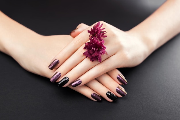 Black and burgundy manicure with flowers on black background Gel nail polish Body care