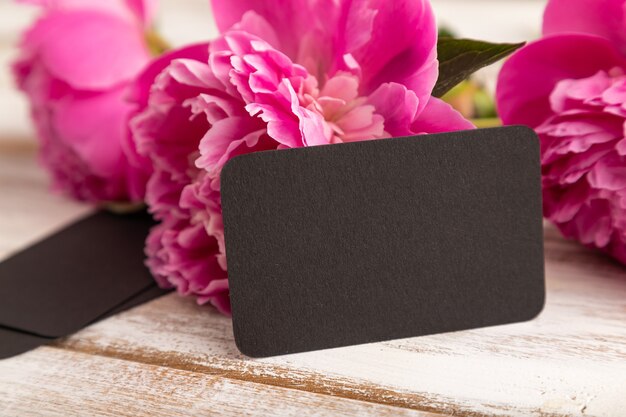 Black business card with pink peony flowers on white wooden background. side view, copy space, 