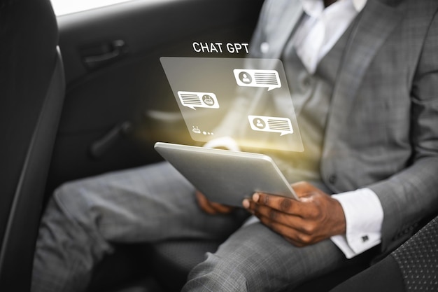 Black businessman sitting in car working on digital tablet cropped