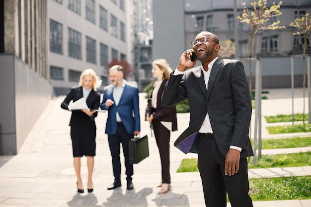 Uomo d'affari nero in piedi e parlare al telefono davanti all'ufficio moderno