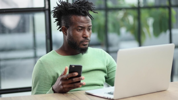 Black businessman talking on a mobile phone in the office while using a laptop