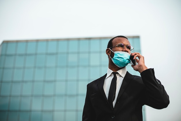 Foto uomo d'affari nero che indossa una maschera di protezione contro la corona di virus con il suo telefono cellulare.