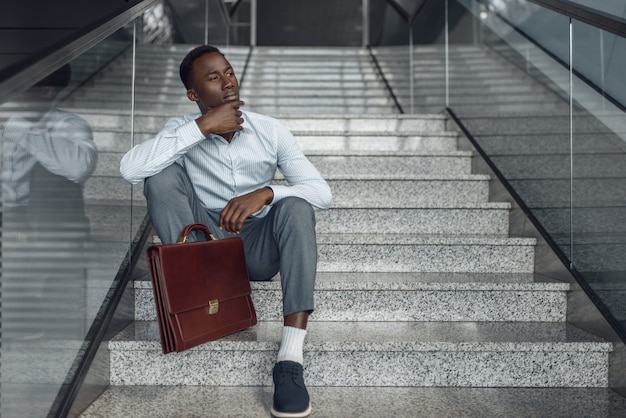 Black businessman with briefcase sitting on stairs