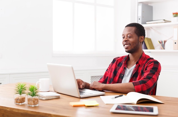 Black businessman working with laptop in modern white office interior. Successful employee at work, copy space