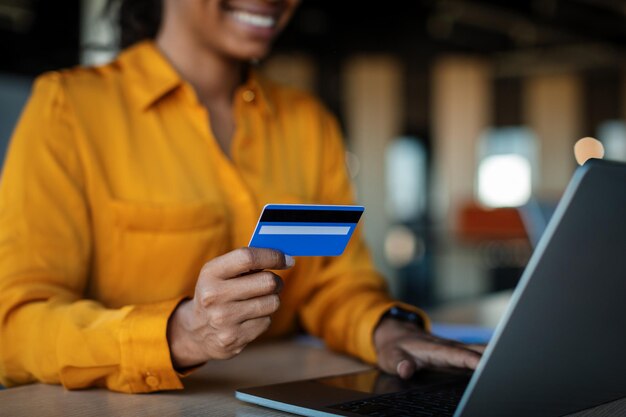 Black businesswoman holding credit card and using laptop for online shopping sitting at workplace in office