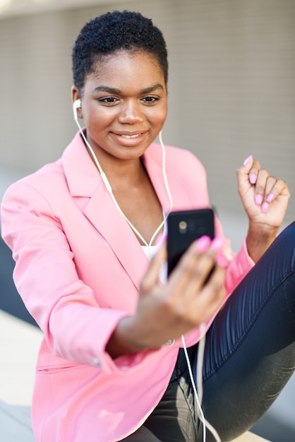 Black businesswoman sitting outdoors speaking via videoconference with her smartphone.