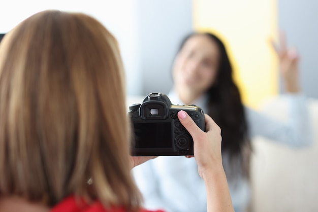 Black camera in hands of woman photographer with woman model in photo studio. Home photo session of friends tfc concept.