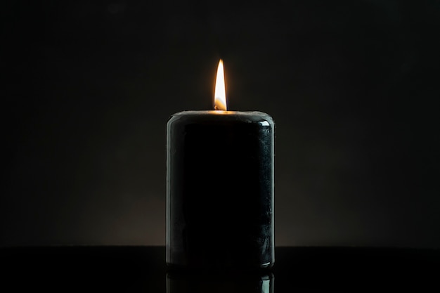 A black candle lit on a black background, esoteric concept