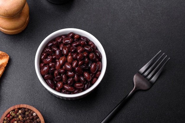 Photo black canned beans in a white saucer against a dark concrete background