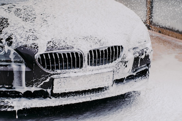 Black car getting wash with soap Car washing concept Automobile at carwash washed by water jet spray Vehicle in foam