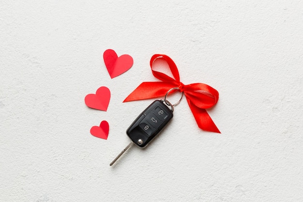 Black car key in a present box with a ribbon and red heart on colored background Valentine day composition Top view