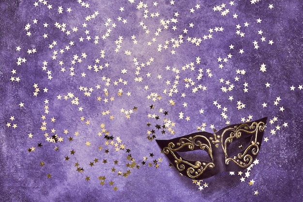 Фото Черная карнавальная маска и золотые звезды на ультрафиолете. вид сверху, копия пространства.