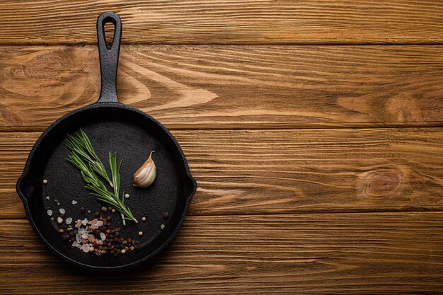 Black cast iron frying pan skillet with food cooking ingredients fresh rosemary garlic salt and pepper