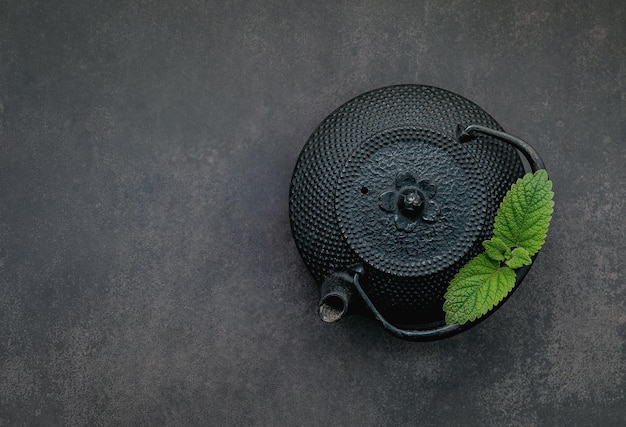 Black cast iron tea pot with herbal tea set up on dark stone background