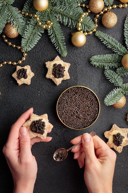 Black caviar appetizers stars in a human's hands on a christmas decorated black table