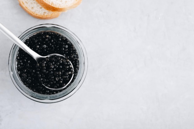 Black caviar in glass jar with spoon on white stone background luxurious delicacy appetizer Top view copy space