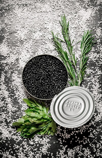 Black caviar in a jar with herbs and salt on the black table salt