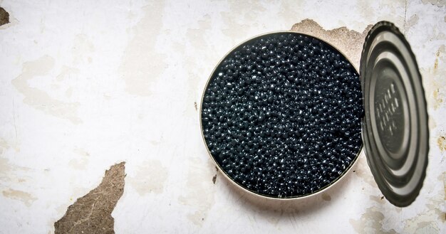 Black caviar in metal can. On rustic table. Free space for text . Top view