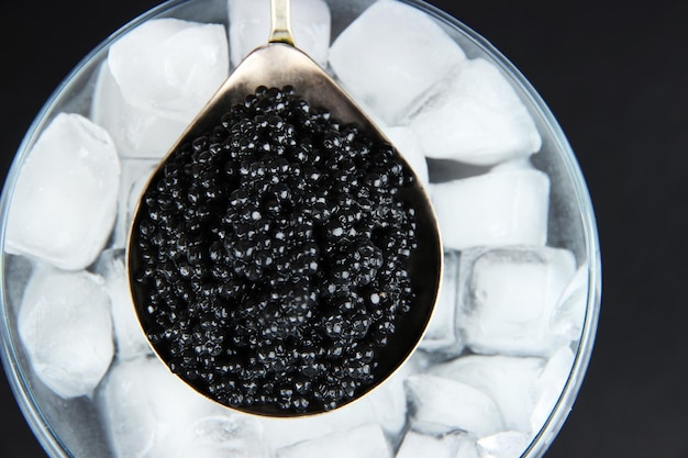 Black caviar in metal dish and ice in glass bowl on grey background closeup