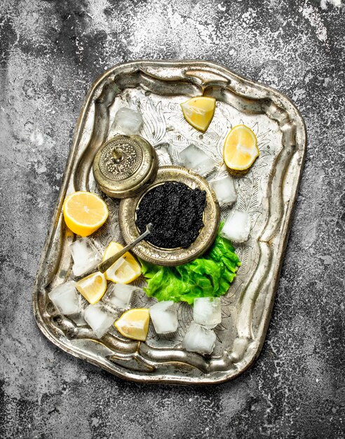 black caviar on the old tray of ice. On rustic background .