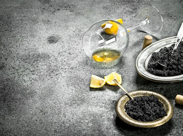 Black caviar with a glass of white wine. On rustic background .