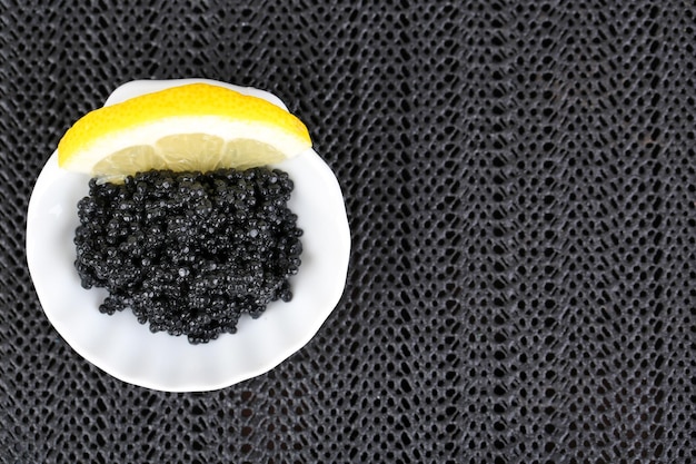 Foto caviale nero con limone su piatto su sfondo tessuto scuro