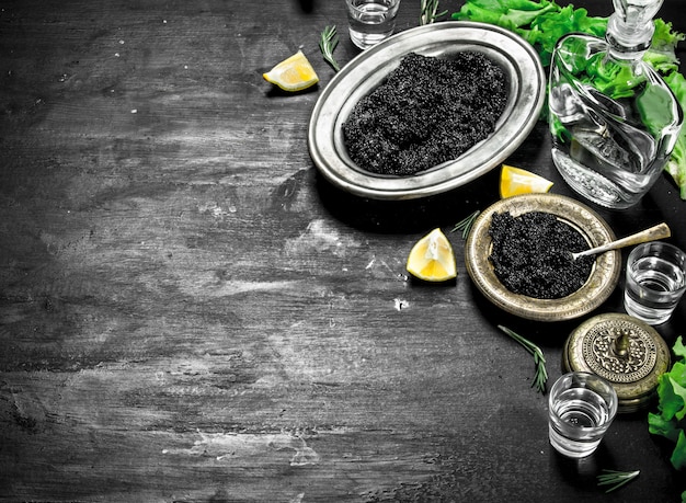 Black caviar with vodka and lemon slices. On a black chalkboard.