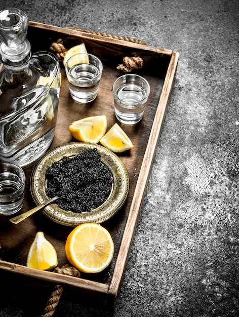 Black caviar with vodka onn old tray on rustic table.