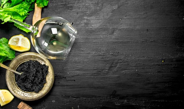 Black caviar with white wine and herbs. On a black chalkboard.