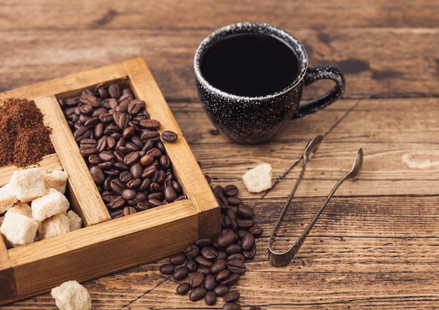 Black ceramic cup of fresh raw organic coffee with beans and ground powder with cane sugar in vintage box on wooden background