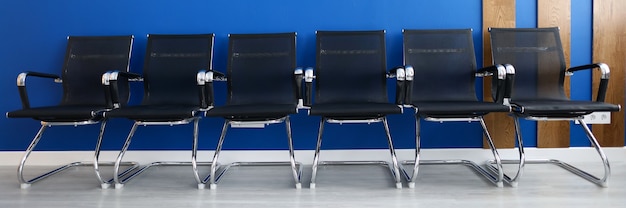 Black chairs on row against blue wall modern office closeup. Business seminar concept