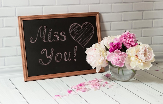 Черная доска с надписью Miss You и сердцем с букетом розовых и белых пионов