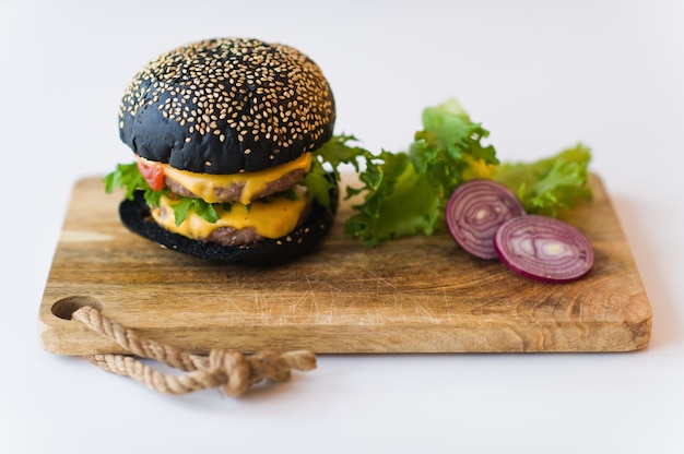 Photo black cheeseburger on wooden chopping board, grey background.