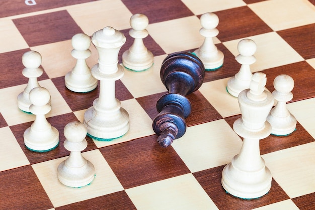 Black chess king surrounded by white pieces