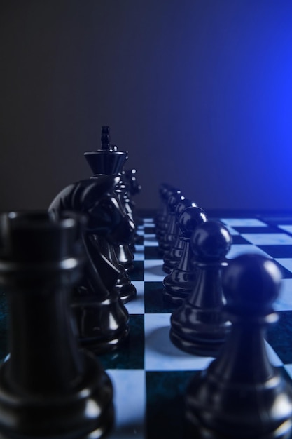 Black chess pieces on chess board with bright blue background light