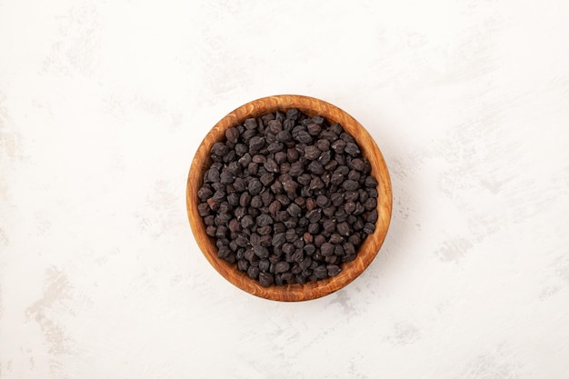 Black chickpeas in wooden bowl on light grey texured background closeup Selective focus copy space