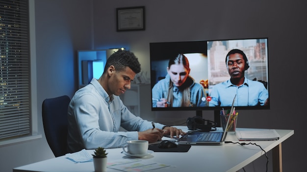 Black chief manager making video call on big monitor with colleagues on quarantine