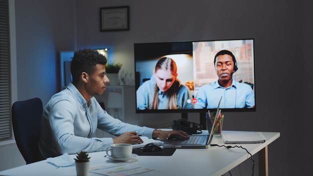 Black chief manager making video call on big monitor with\
colleagues on quarantine