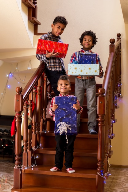 크리스마스 선물을 들고 있는 흑인 어린이 소년들은 계단에서 선물을 들고 모두 치즈 순간이라고 말합니다...