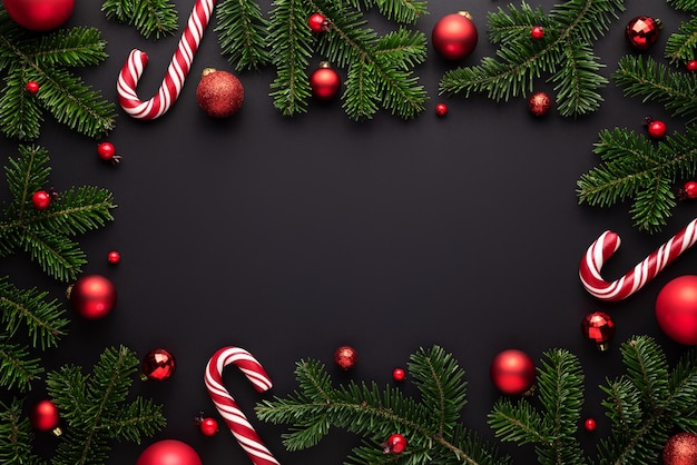 Black Christmas background. Decorative frame of fir branches, Christmas balls and Candy canes