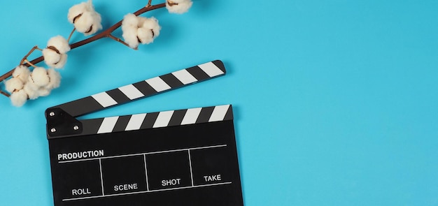 Black clapper board and cotton flowers on blue background