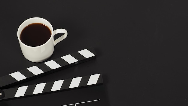 Black Clapper board and hot coffee white cup on black background.