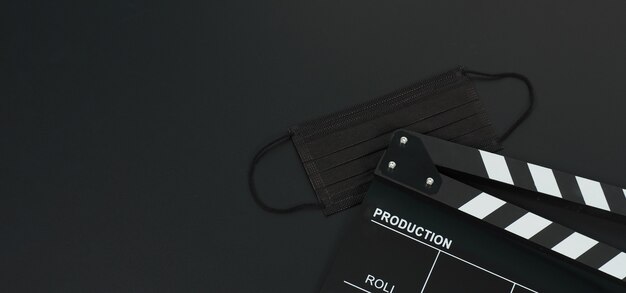 Black Clapper board or movie slate and black face mask on black blackground.