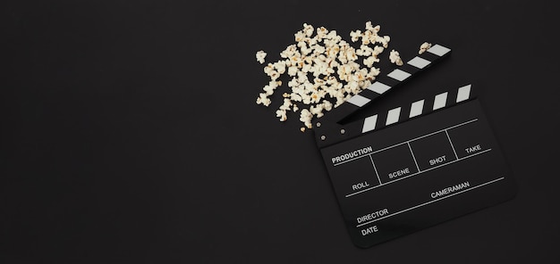 Black clapper board or movie slate and popcorn on black background