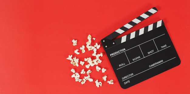 Black clapper board or movie slate and popcorn on a red background.