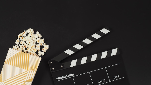 Black clapper board or movie slate and a white box of popcorn on black backgroundx9